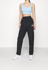 Světle modrý crop top s čtvercovým výstřihem, zkombinovaný s černými, lehkými teplákovými kalhotami s bílým logo Nike, obutý v bílých teniskách.
