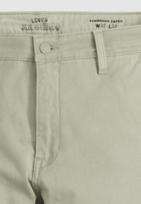 Chino Levi's XX di colore verde chiaro, caratterizzato da un design a gamba affusolata standard, con chiusura a bottone, tasche frontali e dettagli di cucitura minimi.