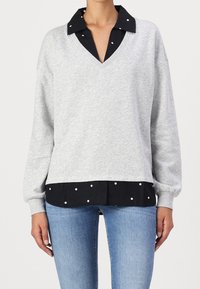 Felpa grigia con scollatura a V e sottile strato nero a pois. Presenta maniche lunghe e una vestibilità comoda. Tessuto strutturato.