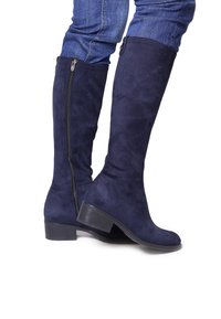 Bottes montantes en faux daim bleu marine avec un petit talon empilé et une fermeture éclair sur le côté. Texture lisse sans motifs ou accents visibles.