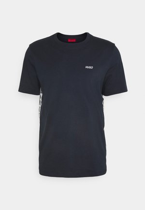 Musta lyhythihainen t-paita, jossa on pieni valkoinen "HUGO"-logo vasemmassa rinnassa ja kuviolliset sivupaneelit.