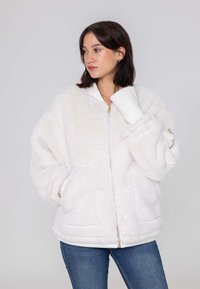Witte nepbont jas met een rits aan de voorkant, geribbelde manchetten en zijzakken. Ontspannen pasvorm met een soepele textuur en minimalistisch ontwerp.