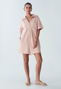 Kratka roza srajčna obleka iz lahkega blaga, z ovratnikom, kratkimi rokavi, žepom na prsih in srebrnimi gumbi. Odprt rob in sproščen kroj.