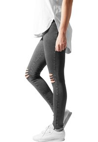 Šedé úzké džíny s roztrhanými detaily, vyrobené z denimu. V kombinaci s volnou bílou košilí a bílými teniskami. Elegantní a přiléhavý design.