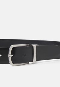 Zwarte leren riem met een gladde textuur, voorzien van een zilveren rechthoekige metalen gesp gegraveerd met "BOSS." Verstelbare lengte met gaatjes.