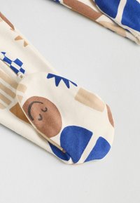 Tejido de crema con patrones geométricos multicolor en azul, marrón y nude. Textura suave, con un diseño de punta redondeada.