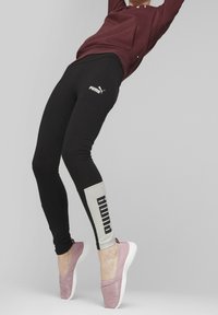 Leggings neri con logo bianco e accenti grigi. Abbinati a scarpe slip-on rosa con tacco testurizzato. Outfit progettato per l'attività fisica.