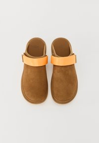 Bruine suède klompen met een oranje textielband. Rond, open achterontwerp; gevoerd voetbed; gladde binnenvoering; minimale stikdetails.
