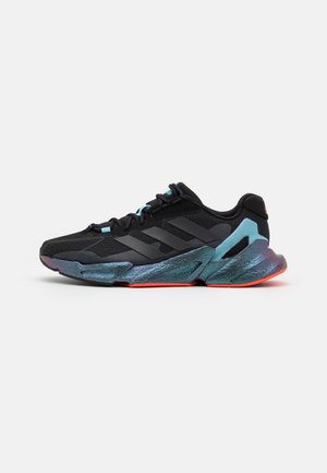 Baskets de sport noires avec tige noire texturée, trois bandes foncées sur le côté, et semelle irisée bleu-vert avec des accents orange sur la semelle extérieure.
