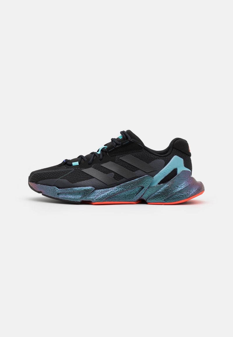 Baskets de sport noires avec tige noire texturée, trois bandes foncées sur le côté, et semelle irisée bleu-vert avec des accents orange sur la semelle extérieure.