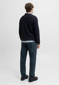 Suéter de punto de color azul marino oscuro con un corte relajado, combinado con pantalones gris oscuro y zapatos negros. El conjunto se lleva sobre una camisa de color azul claro.