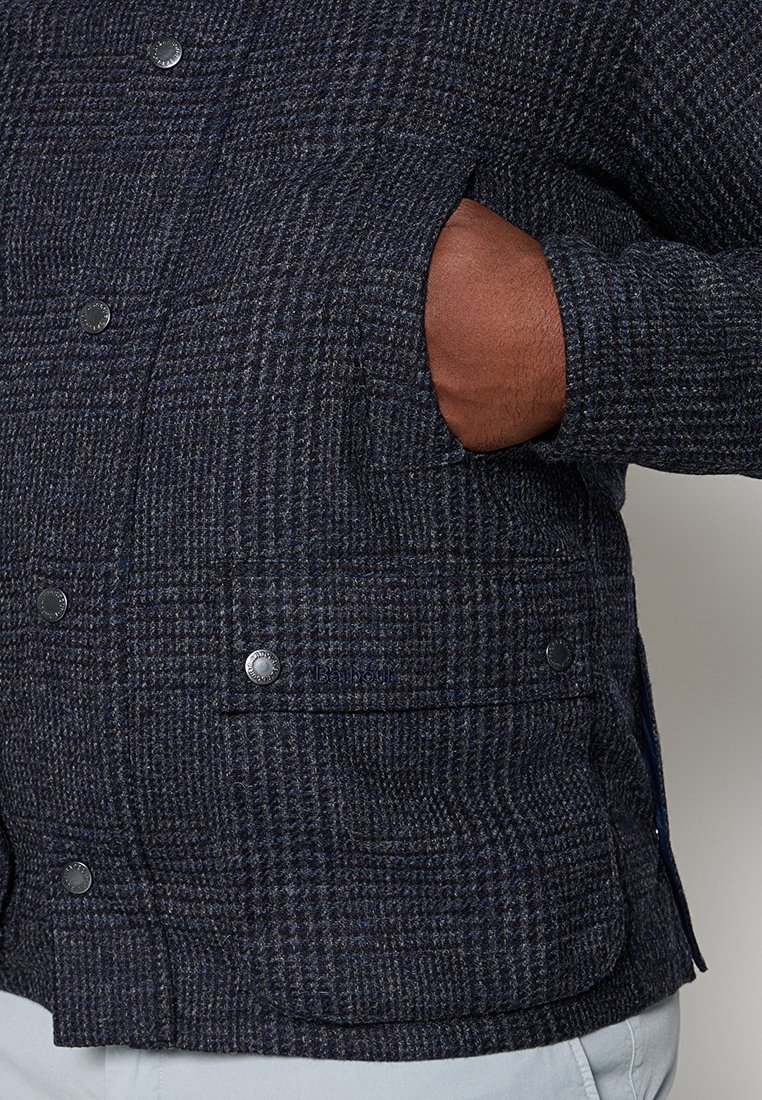 Jacke im Marine-Karo mit strukturiertem Stoff, Knöpfen an der Vorderseite und seitlichen Taschen, die ein lässiges und funktionales Design zeigt.