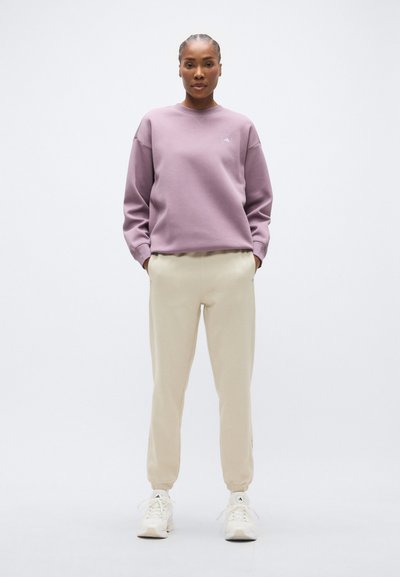 Λιλά φούτερ με στρογγυλή λαιμόκοψη και ριμπ μανσέτες, συνδυασμένο με μπεζ παντελόνι jogger. Άσπρα αθλητικά παπούτσια ολοκληρώνουν την εμφάνιση.