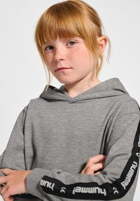Szary hoodie wykonany z miękkiego materiału, z kieszenią na przodzie, sznurkiem do regulacji oraz czarnymi akcentami na rękawach z białymi szczegółami brandingowymi.
