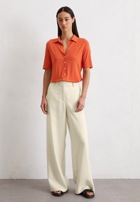Korte mouwen oranje shirt met knopen aan de voorkant, gecombineerd met een brede crème broek. Glad stofmateriaal, eenvoudig kraagontwerp, casual pasvorm.