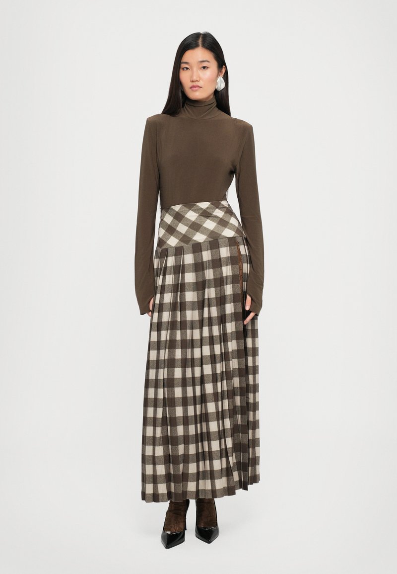 Top de cuello alto marrón ajustado combinado con una falda larga de cuadros que presenta cuadros beige y marrón oscuro, diseño con pliegues y un bolsillo lateral.