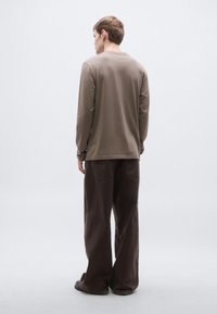 Hosszú ujjú barna ing és bő barna nadrág. Az ing kerek nyakkivágással rendelkezik; a nadrágnak zsebei és bő, laza szabása van. Puha, természetes anyagból készült.