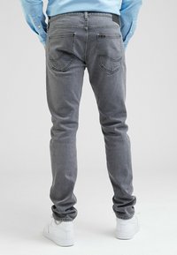 Grå jeans med smal passform, som har bakfickor med böjd sömnad och en svart midjeetikett. Kombinerad med vita sneakers.