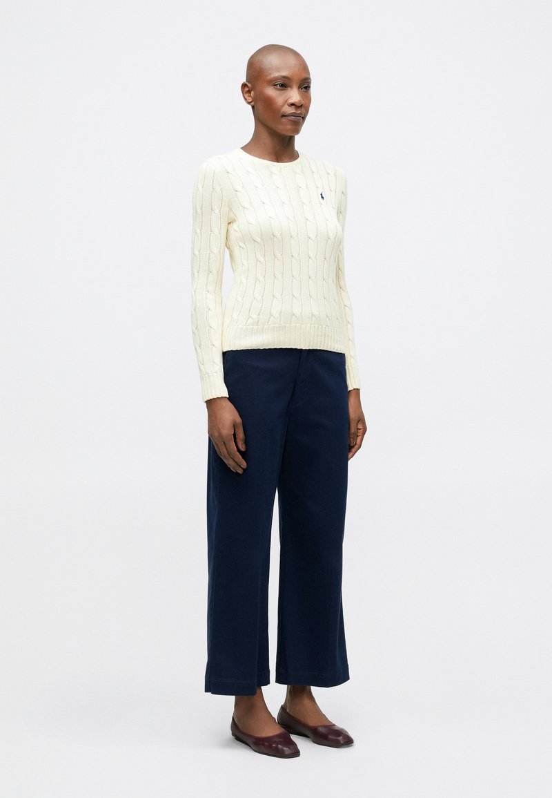 Pull en maille torsadée crème avec des poignets et un ourlet côtelés ; associé à un pantalon large bleu marine et des chaussures plates bordeaux. Design minimaliste.