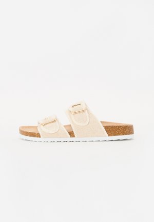 Beige slip-on sandal med to justerbare stofstropper og gyldne spænder, kork-fodseng og hvid tekstureret gummisål.