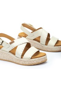 Sandales en cuir blanc avec des brides croisées, semelle intérieure rembourrée et semelle en wedge texturée. Comprend une fermeture à boucle réglable et des accents perforés.