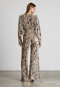 Mono de manga larga con estampado de serpiente en beige y marrón, que presenta una cintura ajustada y un diseño de pierna ancha. Textura suave con un acabado brillante.