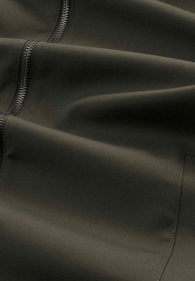 Mørkeolivenfarvet stof med en glat overflade og synlige sorte lynlåse, der har et slankt og minimalistisk design.