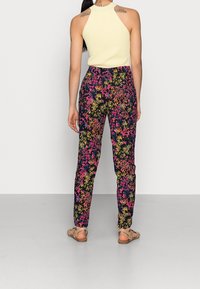 Blommönstrade byxor i svart med flerfärgade blommor, tapered design och hög midja, kombinerat med en lätt, figurnära tanktop.