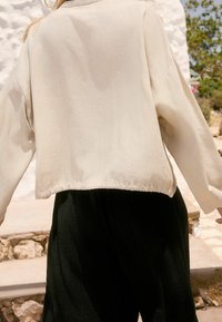 Lichtbeige cropped jasje met een ontspannen pasvorm, gemaakt van zachte stof. Heeft verlaagde schouders en een zoom met een geraffineerd detail.