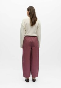 Cream knitted sweater with a round neckline, paired with wide maroon pants featuring an elastic waistband and side pockets. Brown shoes.