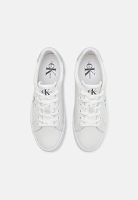 White leather sneakers with lace-up design, flat rubber soles, logo detailing on the side and tongue, and smooth texture.