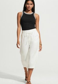 Fekete bordás ujjatlan felső fehér díszítéssel, laza fehér vászon nadrággal, amelynek kényelmes derékpántja és húzózsinórja van.