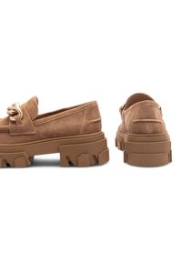 Hnedé nubukové mokasíny s hrubou gumovou podrážkou, s dekoratívnym zlatým reťazcom na vrchu. Textúrovaný povrch a moderný tvar.