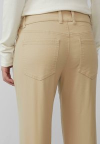 Beige highwaisted broeken met twee achterzakken, gestikte details en een gladde textuur. De stof lijkt zacht en licht rekbaar.
