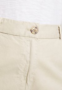 Pantaloni in cotone beige con vestibilità classica, chiusura a un bottone e cuciture visibili lungo le cuciture.