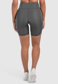Hoge taille, donkergrijze sportshorts met een gladde, elastische textuur, die tot halverwege de dij reiken; gecombineerd met witte sportschoenen.