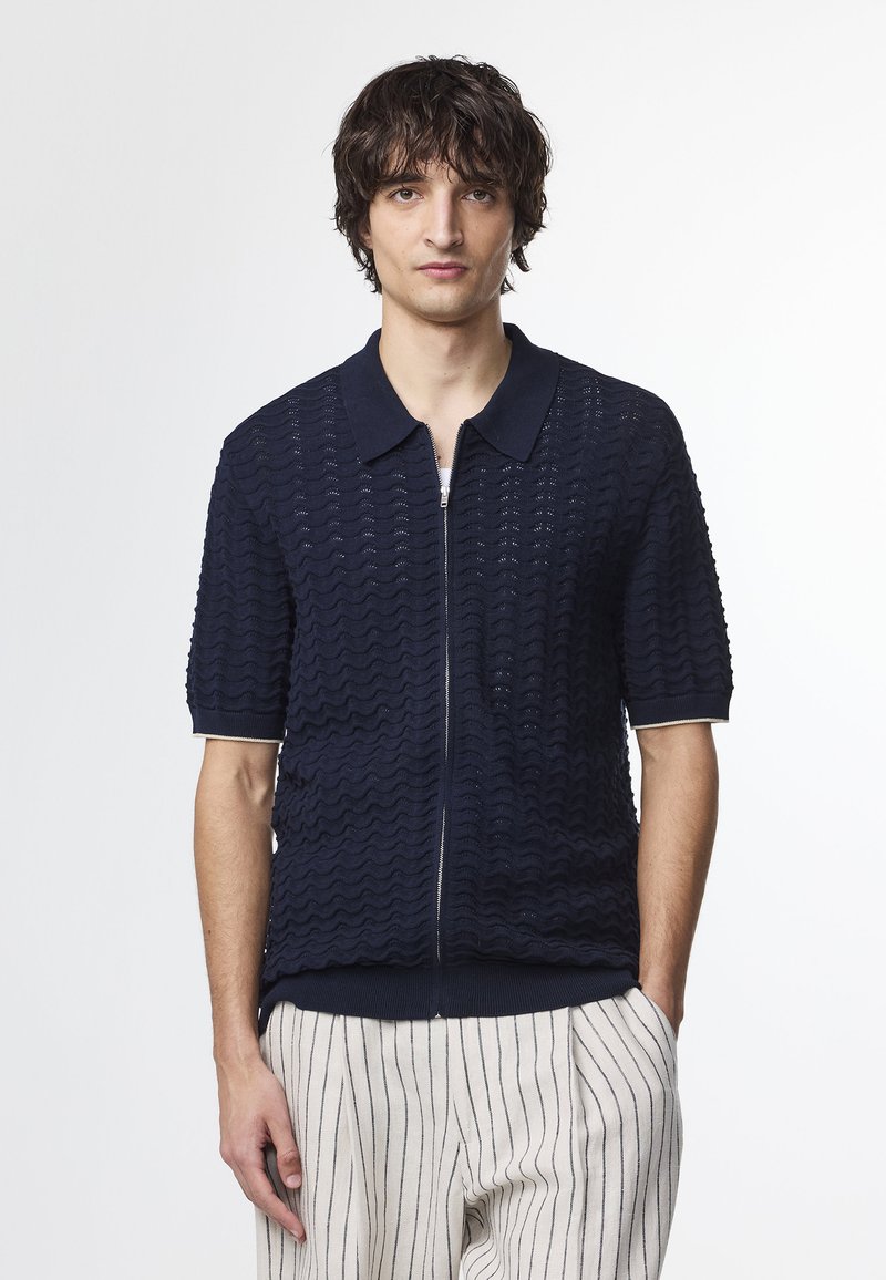 Mørkeblå kortærmet zip-up sweater med en bølget teksturmønster, ribbet krave og manchetter, parret med stribede bukser.