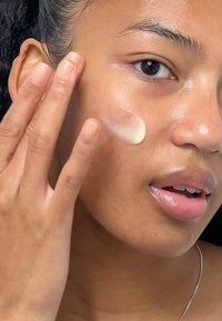 Une crème hydratante est appliquée sur la peau. La crème est de couleur claire, avec une texture lisse, sur un teint de peau claire et éclatante.