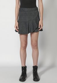 Falda a cuadros gris con dobladillo acampanado, que presenta un diseño asimétrico. Llevada con botas de tobillo negras con cordones. Textura suave.