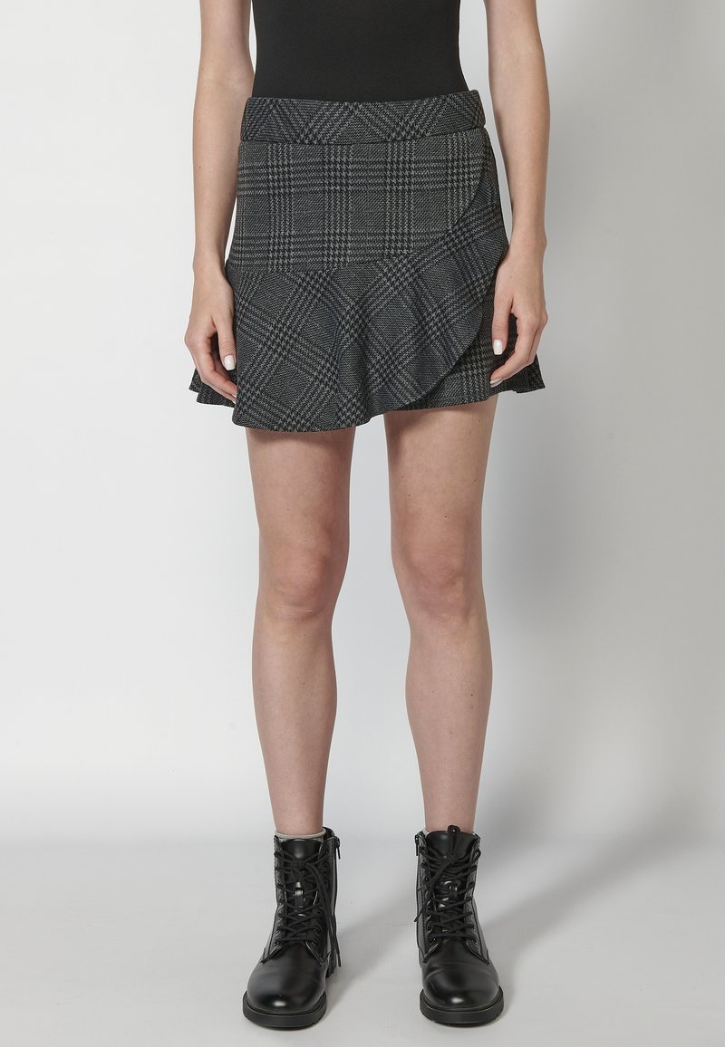 Falda a cuadros gris con dobladillo acampanado, que presenta un diseño asimétrico. Llevada con botas de tobillo negras con cordones. Textura suave.