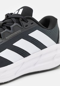 Black athletic shoe with white stripes, textured upper, padded collar, and a white outsole, features branding on the heel and tongue.