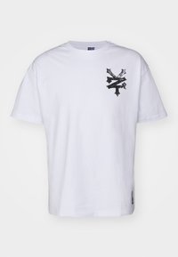 Hvid bomulds t-shirt med korte ærmer, prydet med et sort grafikdesign på venstre brystområde og en lille brandlabel ved kanten.