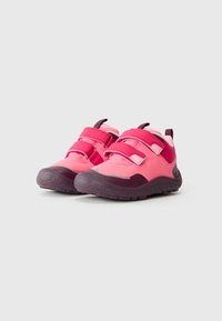 Sneakers rosa per bambini con suole scure e due cinturini in velcro, posizionati uno accanto all'altro su uno sfondo chiaro uniforme.