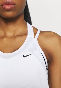 Woman wearing white Nike tank top with visible shoulder and upper chest against plain background.