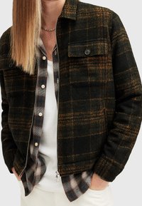 Jaqueta s padrovaným zipem v tmavě zelené a oranžové barvě, vyrobená z vlněné směsi. Obsahuje náprsní kapsu, knoflíkovou légu a texturovanou tkaninu.