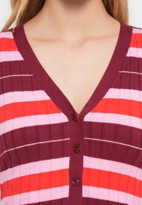 Ριγέ ζακέτα σε αποχρώσεις του ροζ, κόκκινου και μπουρντό, με V-λαιμόκοψη, ριμπ υφή και πέντε κουμπιά στο μπροστινό μέρος.