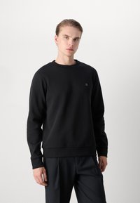 Black crewneck sweatshirt featuring long sleeves, a ribbed neckline, and subtle logo detailing on the chest, made from a soft fabric.