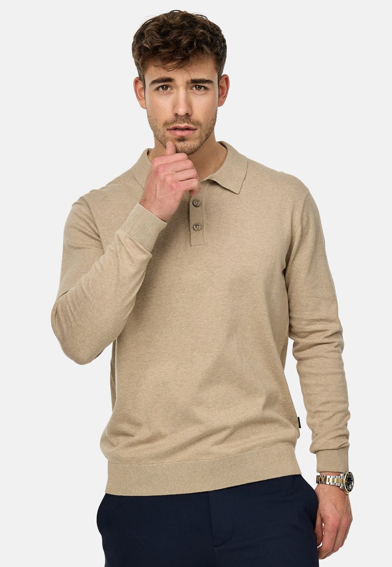Polo beige à manches longues avec col, patte de boutonnage à trois boutons, poignets côtelés et ourlet droit. Tissu texturé avec un subtil détail de motif.