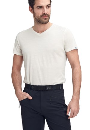 Kremowa, krótko rękawowa koszulka typu v-neck z teksturowanej tkaniny. Noszona z czarnymi spodniami z kieszenią na zamek i paskiem.