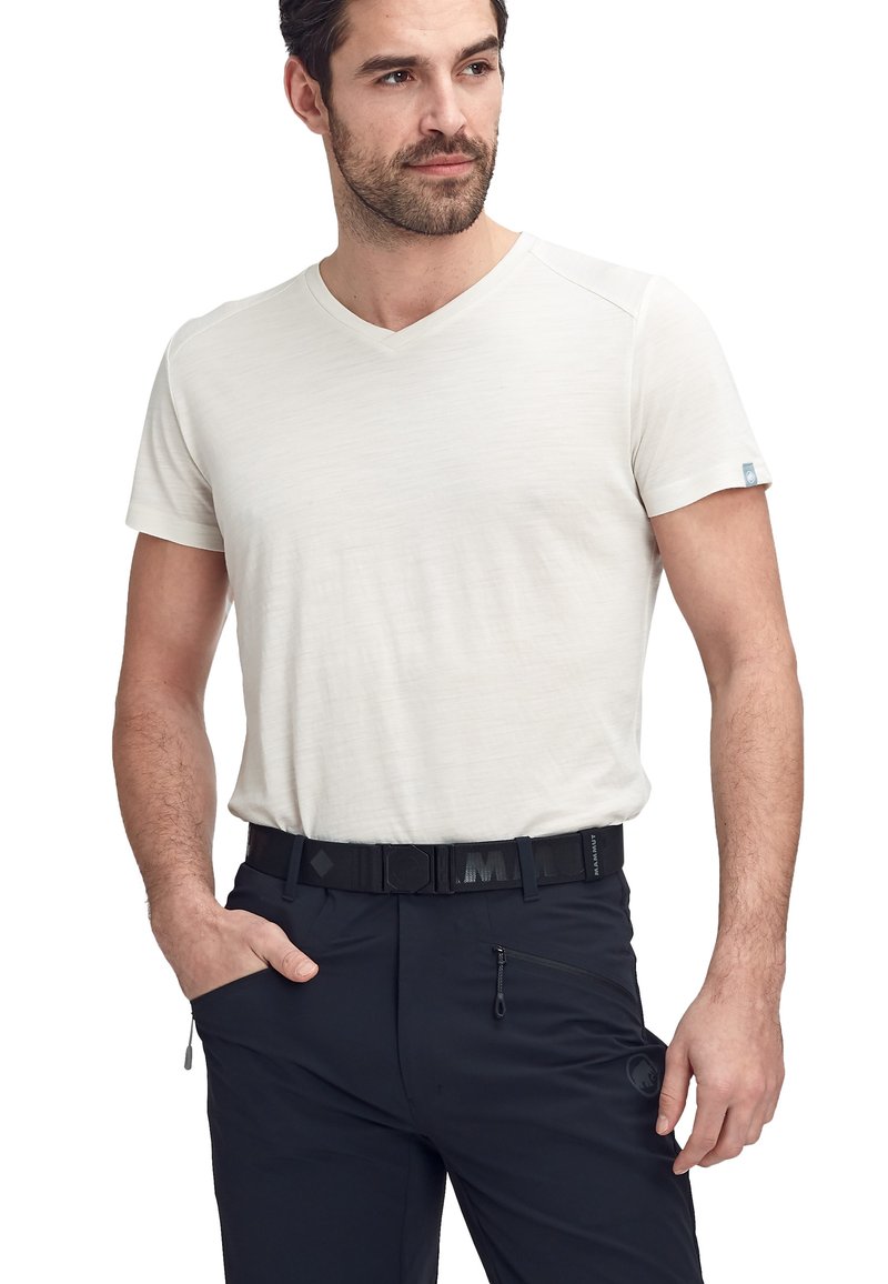 Crème-kleurig, kort mouw v-hals t-shirt van een gestructureerde stof. Gecombineerd met zwarte broek met een ritszak en riem.
